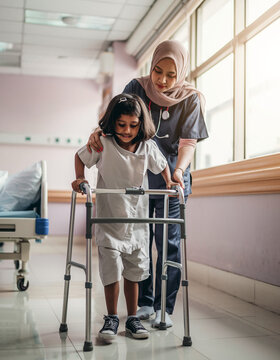 A Muslim nurse supports a child during physical rehabilitation with a walking aid in the hospital.