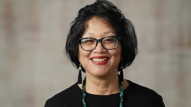 A woman with short dark hair and a warm smile wearing a white sweater and dangling earrings against a blurred background