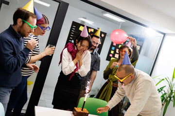 Business team celebrates birthday with cake and party hats in modern office setting during work hours