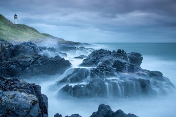 Misty Waves and a Guiding Lighthouse on a Rocky Coast