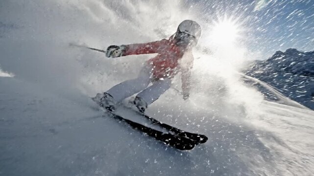Dynamic shot of skier in orange jacket skiing fast down slope with snow spray against sun. Perfect for winter sports, travel concepts and active lifestyle promotion.