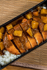 A rectangular plate of white rice topped with crispy pork cutlet and rich curry sauce with diced vegetables.