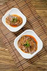 Two plates of thin beef slices served in spicy chili oil garnished with sesame seeds and green herbs.