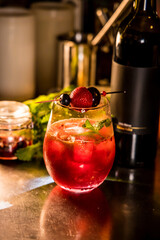 A glass of red berry cocktail garnished with fresh berries and mint leaves placed beside a wine bottle.