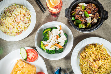 A table set with multiple Chinese dishes including fried rice, noodles, stir fried vegetables, and clay pot meat.