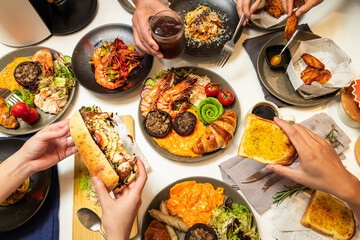 A table filled with various brunch dishes including croissants, eggs, grilled vegetables, shrimp, and drinks.