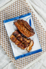 A rectangular plate of grilled pork slices arranged neatly on a white ceramic dish with garnish.