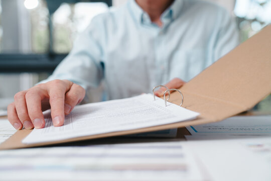 Business professional reviewing documents in a folder at an office desk. Concept of paperwork, administration, contract review, compliance, auditing, and corporate documentation process.
