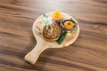 A wooden board with assorted Japanese dishes including grilled rice cake, vegetables, and dipping sauce.