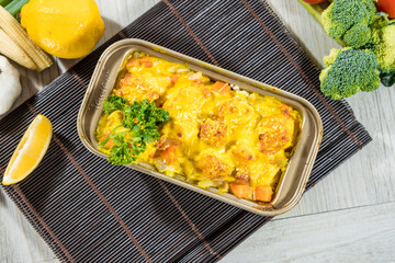 A rectangular tray of baked meatballs topped with melted cheese surrounded by fresh vegetables.