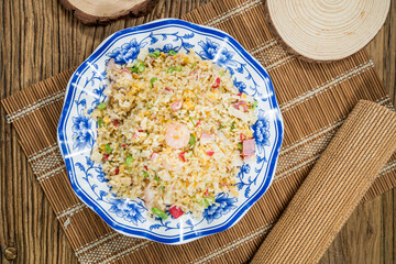 A blue floral plate filled with fried rice mixed with shrimp, diced vegetables, and egg, placed on a wooden mat for a rustic look.