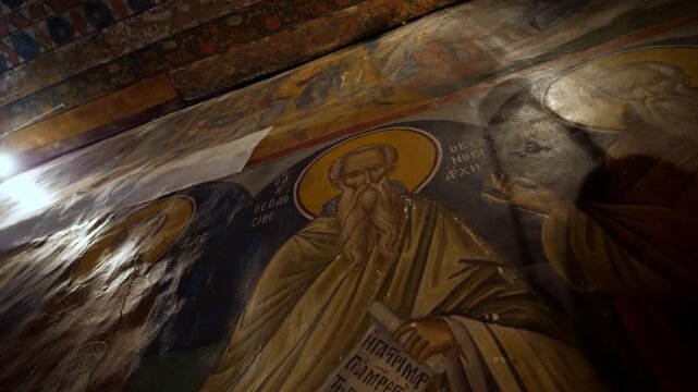 Interior view of an ancient Eastern Orthodox monastery in Meteora, Greece, showcasing beautifully preserved Byzantine frescoes. The hagiography depicts saints and biblical figures
