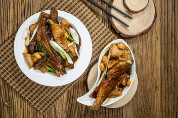 Two plates of braised fish fillets cooked in rich soy-based sauce with garlic cloves and green onion, served on wooden table with chopsticks.