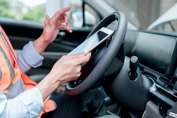 Driver using a smartphone inside a car while wearing a safety vest. Concept of distracted driving, road safety, mobile phone usage, transportation risk, insurance awareness.