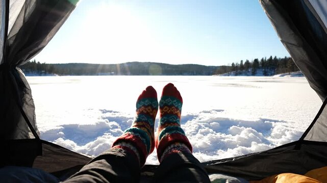 POV shot of feet in warm wool socks resting in tent looking at snowy winter landscape. Concept of adventure and cozy camping. Great for travel and outdoor recreation themes.