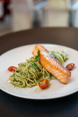 Parsley pesto pasta with grilled salmon and cherry tomato, served on plate