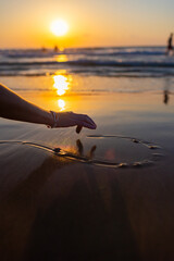 A girl draws a heart in the wet sand. Draw with your finger in the sand. Happy Valentine's Day. A woman draws a love symbol in the smooth sand.