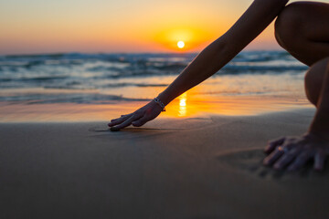 A girl sits by the sea and draws on the wet sand. A woman draws a heart with her hand on the beach. Valentine's Day.