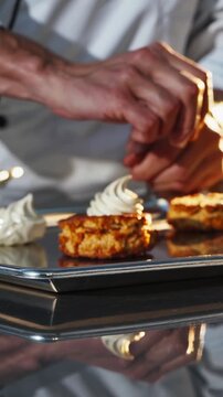Pastry chef decorating small cakes with white cream using a piping bag, in a professional kitchen with warm lighting, creating a visually appealing dessert