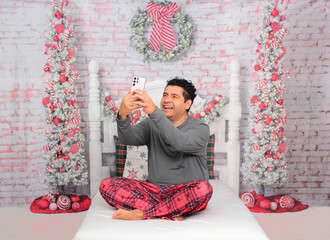 Dark-skinned Latino adult man uses his cell phone to make calls, send messages, and shop while celebrating Christmas remotely and alone