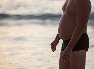 A man with a large belly is standing on the beach