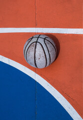 A weathered basketball sits in stark contrast against the vibrant orange and blue expanse of the court, defined by crisp white lines.