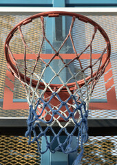 Framed by a steel grid fence, an orange metal basketball rim and net are set against a fiberglass basketball backboard. Space for text.
