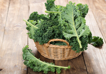 Fresh kale leaves in a wicker basket on a wooden table