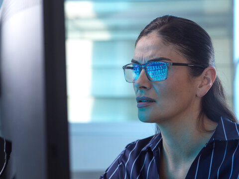 Businesswoman in office looking at computer screen with code reflection