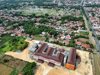 Aerial View of Suburban Residential Area with Green Rice Fields and Main Road in Indonesia