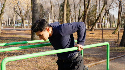 Determined man performing dips on parallel bars outside.