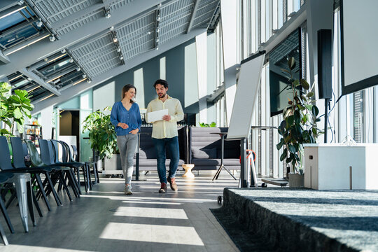 Businessman and businesswoman discussing over tablet PC and walking in office