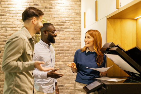 Coworkers in an office using a copy machine and smiling while talking