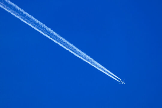 Airplane flying with contrail in blue sky above Germany
