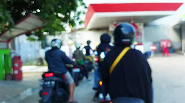 Blurred image of motorcyclists queuing at a gas station in Indonesia under bright daylight.