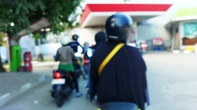Blurred image of motorcyclists queuing at a gas station in Indonesia under bright daylight.