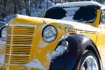 Close up view of an yellow and black retro car against the backdrop of a winter forest