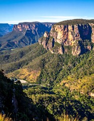 Naklejka premium Stunning vista of a mountainous terrain under a clear blue sky. Rugged cliffs meet lush green valleys
