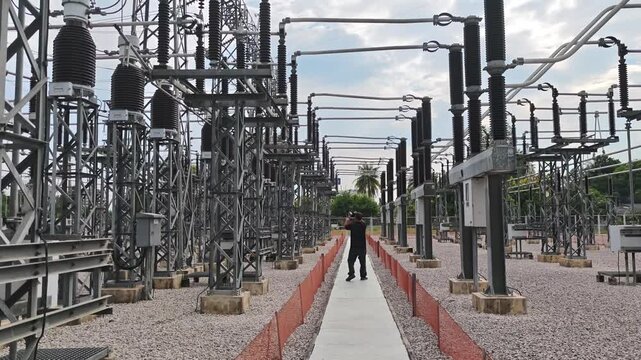 Electrical engineer walking and inspecting high voltage substation switchyard equipment.