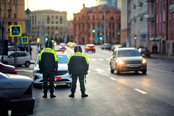 Two police officers in visibility uniforms standing near patrol car, monitoring passing traffic and...