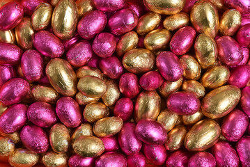 Large & small pink and gold foil wrapped chocolate easter eggs, against a peach orange background.
