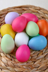 Brightly colored easter eggs, in a natural straw basket against a natural white background.