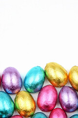 Pile of foil wrapped chocolate easter eggs in pink, blue & lime green with a white background.