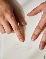 Close-up of hands reading braille on white paper, soft shadows, minimal background, elegant stock-style composition, symbolizing accessibility, inclusion, and tactile literacy