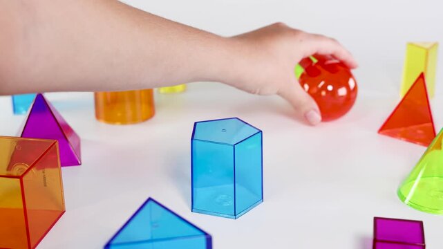Hand Placing a Red Sphere on a Blue Hexagonal Prism