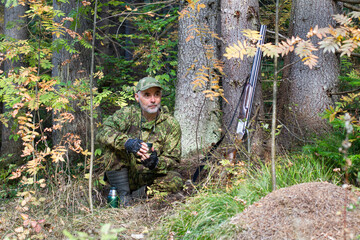 A hunter drinks tea in the forest next to an anthill