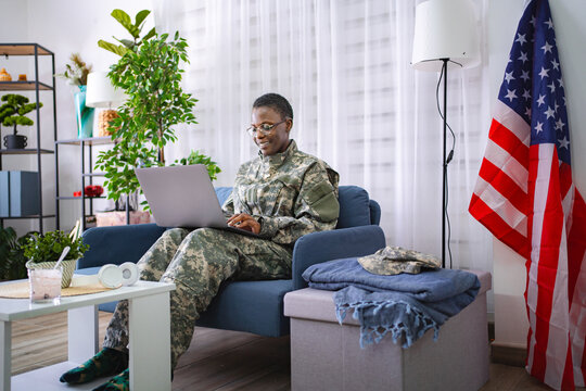 Female soldier sitting on sofa using laptop with United States flag in background