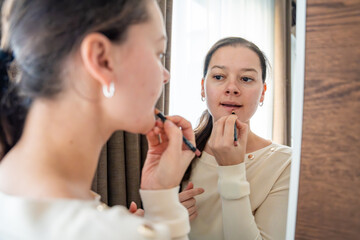 Young woman applying lipstick in front of mirror as part of her beauty routine.