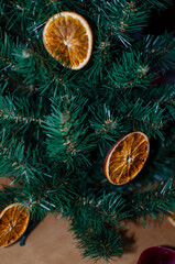 A close-up of a dried orange slice hanging as a festive ornament on a lush green Christmas tree. The slice is beautifully dehydrated, with rich amber-orange hues, translucent segments.