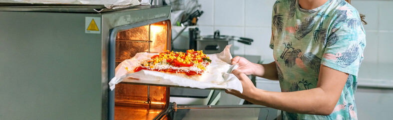 Banner of unrecognizable female chef skillfully putting a freshly pizza to bake in professional oven in a commercial kitchen, expertly preparing a delicious meal for eager customers